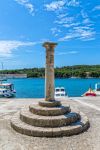 Colonna e basamento rotondo in pietra al porto di Prvic Luka in estate, isola di Prvic, Croazia.
