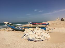Due tradizionali barche in legno sul litorale nei pressi di Nouakchott, Mauritania. In primo piano, reti da pesca e sullo sfondo alcune abitazioni - © Senderistas / Shutterstock.com