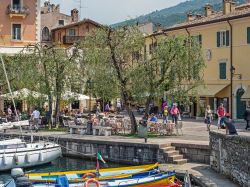Il vecchio porto di Torri del Benaco, provincia di Verona. Sullo sfondo, uno scorcio del centro storico con edifici e turisti - © 167880122 / Shutterstock.com