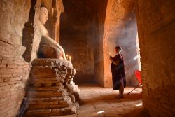 In preghiera al tempio buddhista di Bagan, Myanmar. In piedi dinnanzi alla statua del Buddha, questo giovane monaco prega rischiarato solo dalla luce di una candela - © jiraphoto / Shutterstock.com ...