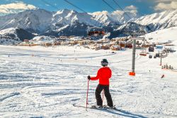 Lo ski resort dell'Alpe d'Huez, Francia, in inverno con la neve. In primo piano, uno sciatore pronto ad affrontare le piste innevate.

