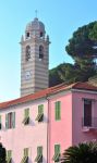 Un campanile di Celle Ligure, Liguria, dietro a un edificio tinteggiato nelle sfumature del rosa.
