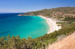 Una spiaggia di Solanas con sabbia bianca, colline con vegetazione, mare blu e il piccolo villaggio, frazione del Comune di Sinnai, Sardegna.



