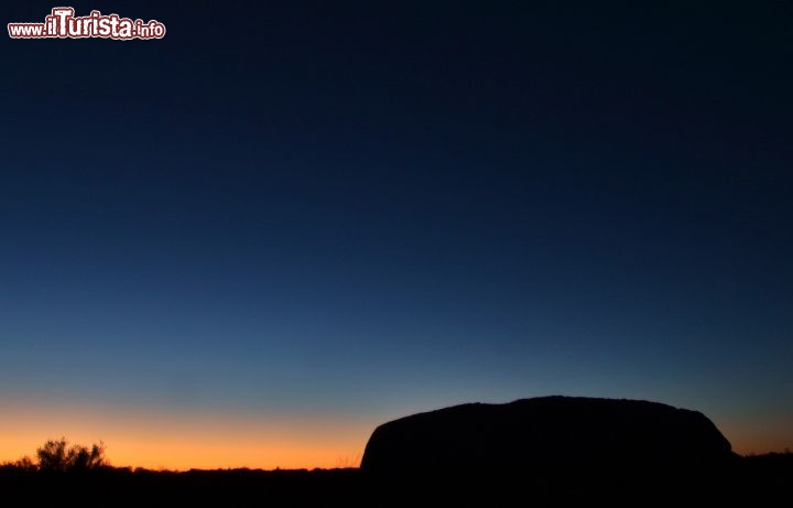 Immagine Crepuscolo mattutino ad Ayers Rock in Australia - La montagna sacra di Uluru appare magica ad ogni momento della giornata! Anche ben prima dell'alba, quando la notte lascia spazio ai colori del crepuscolo all'orizzonte, la montagna, con il suo semplice profilo, cattura in modo magnetico lo sguardo dei viaggiatori! Una presenza davvero dal grande fascino, che interroga le persone nell'intimo del loro cuore