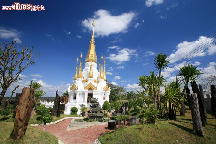 Immagine Pagoda Wat Tham Kuha Sawan a Ubon Ratchathani  - Le guglie dorate di questo tempio dedicato alla fede buddhista si innalzano dalla base in muratura bianca in direzione del cielo blu intenso. A creare una suggestiva cornice, in cui protagonista assoluto è lo stupa, non manca neppure la vegetazione rigogliosa che con il suo verde brillante crea un variegato gioco di colori © Blanscape / Shutterstock.com