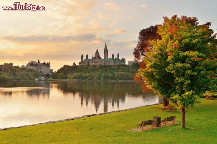 Immagine A Ottawa, capitale del Canada nella provincia dell'Ontario, gli spazi verdi e i giardini pubblici sono numerosi. Nell'immagine il fiume Ottawa, un prato curato, i colori dell'autunno e sullo sfondo la Parliament Hill con gli edifici del Parlamento - © Songquan Deng / Shutterstock.com