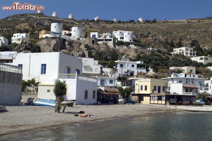 Immagine La spiaggia di Pandeli a Leros, con i mulini a vento a fare da suggestiva cornice sullo sfondo. Le case bianche e dalle tonalità pastello rendono unico questo villaggio greco composto prevalentemente da una popolazione dedita alla pesca - © fritz16 / Shutterstock.com