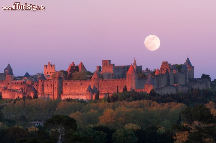 Immagine Tramonto a Carcassonne (Francia del Sud) con la luna piena che occhieggia alla spalle del borgo. Mentre il sole si congeda le pietre delle mura, costruite a partire dall'età romana e ampliate nel medioevo, si tingono di rosa e di viola  - © Paul Palau