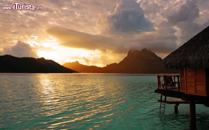 Immagine Un'alba spettacolare all'Isola di Bora Bora, nella Polinesia Francese. Chi alloggia in uno dei famosi resort su palafitte dovrebbe svegliarsi preso almeno una volta, per lanciare uno sguardo fuori dalla finestra e ammirare il gioco di luci del sole nascente sul mare - © wilar / Shutterstock.com