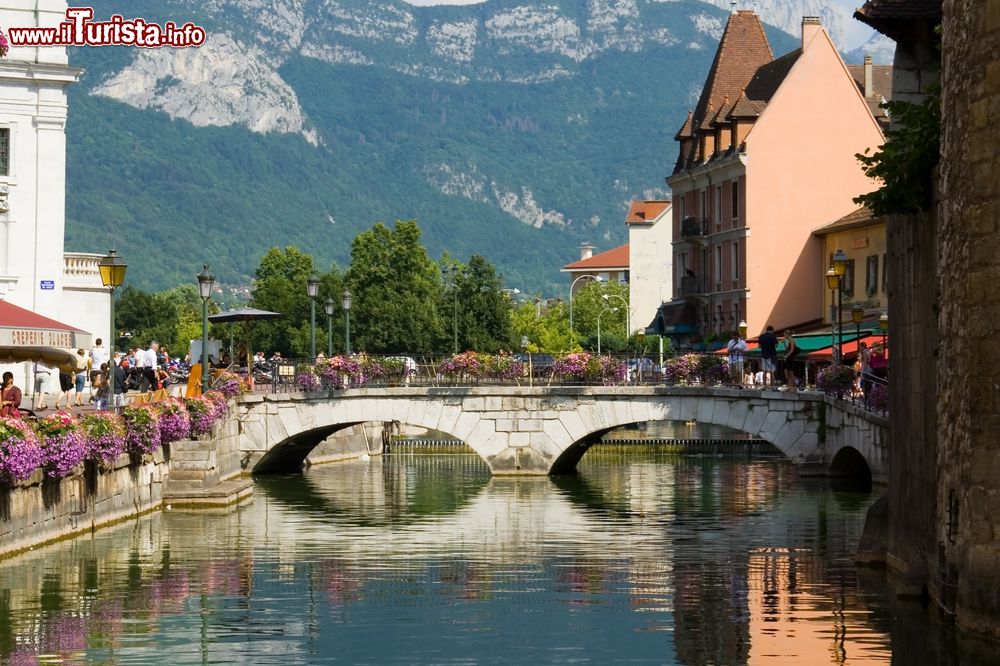 Immagine Antichi palazzi affacciati su un canale di Annecy, Francia. Sullo sfondo le cime delle montagne che fanno da cornice alle acque blu scuro.