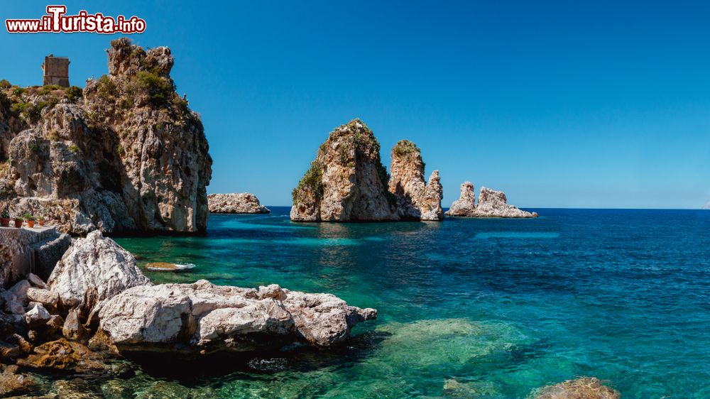 Immagine Faraglioni di Scopello, Sicilia: queste formazioni rocciose emergono dall'acqua cristallina del mare, proprio di fronte all'antica tonnara, caratterizzando l'intero paesaggio.