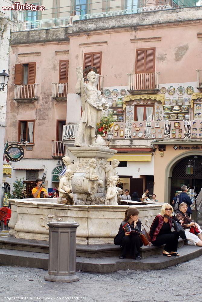 Immagine Fontana in una piazza di Amalfi con persone sedute sugli scalini, Campania. Sullo sfondo, negozi di souvenir e botteghe - © Angela N Perryman / Shutterstock.com