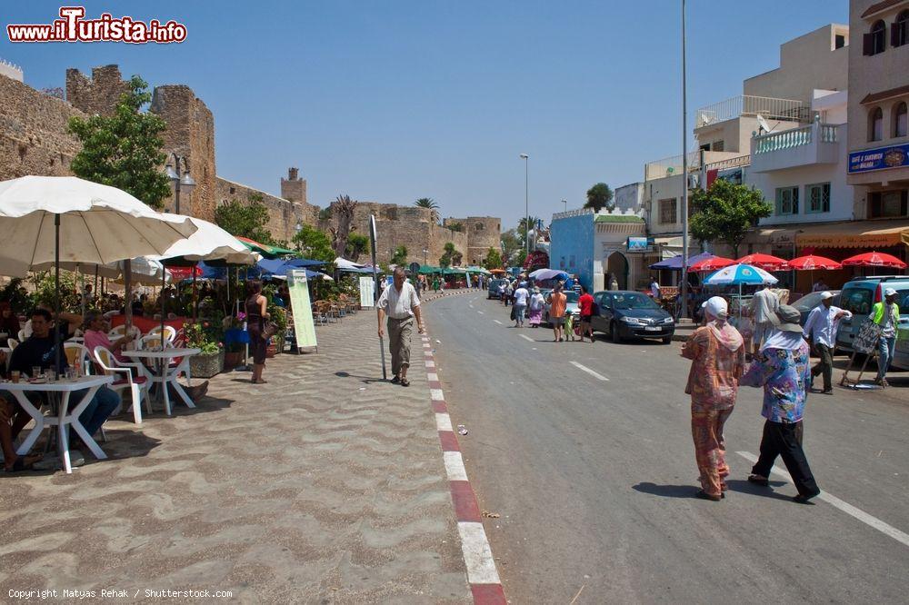 Immagine Gente a spasso per le strade di Asilah, Marocco. Asilah è una cittadina fortificata nel nord del Marocco, a circa 46 km da Tangeri. Nel 1471 fu conquistata dai portoghesi che la occuparono sino al 1550 quando dovettero abbandonarla per via della crisi economica - © Matyas Rehak / Shutterstock.com