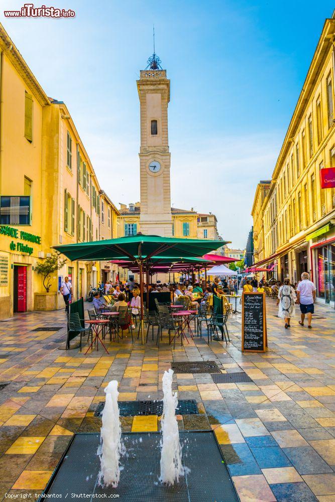 Immagine Gente ai tavolini di un bar nel centro di Nimes, Francia. Sullo sfondo, la torre dell'orologio - © trabantos / Shutterstock.com