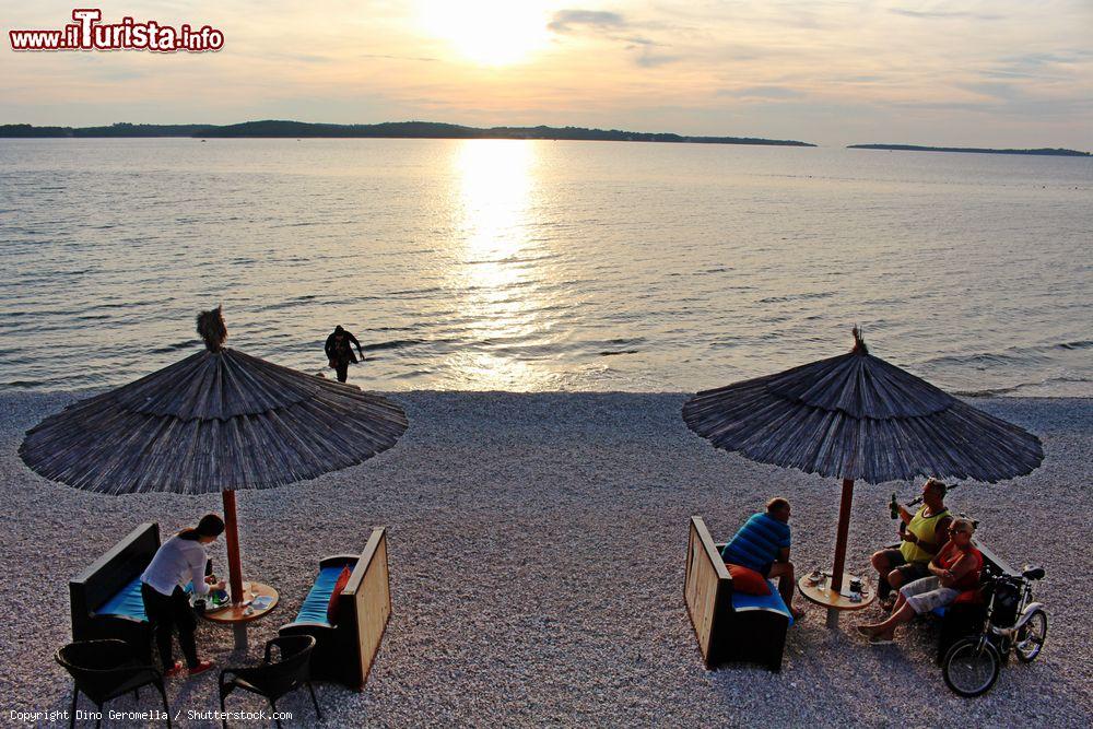 Immagine Gente in relax al tramonto sulla spiaggia di Fazana, di fronte alle isole Brioni, Croazia - © Dino Geromella / Shutterstock.com