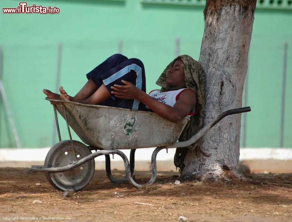 Immagine Un giovane ragazzo riposa seduto in una carriola a Luanda, Angola, all'ombra di un albero - © terezinhka / Shutterstock.com