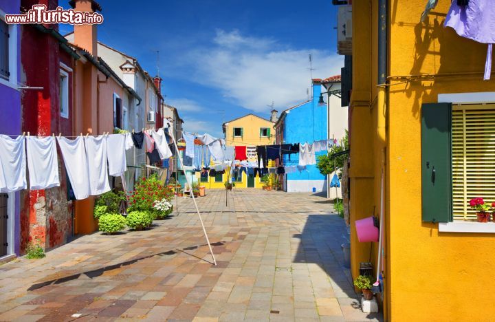 Immagine I panni stesi nelle strade di Burano: un'isola dove le antiche tradizioni non muoiono mai - a Burano, così come negli angoli meno turistici della bella Venezia, è ancora usanza comune stendere i panni al sole attraverso un filo legato da una casa all'altra. Si tratta di usanze popolari, di una volta, ma che in questo piccolo angolo un po' isolato d'Italia sono nient'altro che vita quotidiana. - © arhimax / Shutterstock.com