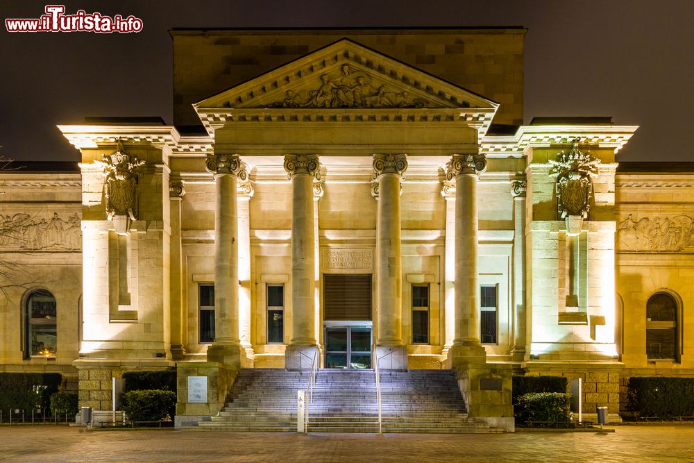 Immagine La facciata della biblioteca di Wuppertal, Germania, fotografata di notte. L'architettura è tipicamente in stile greco antico con quattro colonne che sorreggono il frontone decorato.