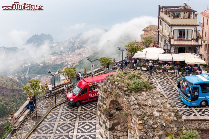 Immagine La piazza di Castelmola con i bus turistici, Sicilia. Costruita nel 1954, piazza Sant'Antonio è il belvedere sulla sottostante Taormina, in questa immagine fotografata sotto un cielo carico di nubi di pioggia. Particolarmente caratteristica è la pavimentazione a mosaico in pietra bianca e lavica della piazza su cui si affaccia anche la chiesa che conserva intatti i tratti dell'architettura religiosa del sud Italia. Recentemente è stata trasformata in Auditorium comunale -  © T.W. van Urk / Shutterstock.com 