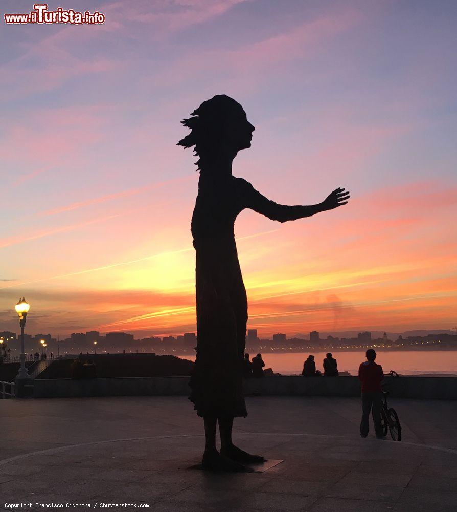 Immagine Monumento alle madri dei migranti sulla passeggiata di Gijon, Spagna: una suggestiva veduta della scultura in bronzo fotografata al tramonto - © Francisco Cidoncha / Shutterstock.com