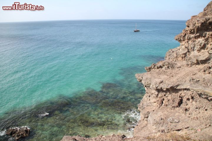 Immagine Veduta dell'acqua turchese di Morro Jable fotografata dalla costa, Fuerteventura, Spagna - Conosciuta anche come Barcelò Jandia Playa, in realtà nel linguaggio più comune è definita la spiaggia di Morro Jable. Qui, dal basso così come dall'alto come nel caso di questa immagine, si possono vedere dei panorami bellissimi, soprattutto quelli che affacciano sull'acqua turchese e regalano una visione di relax e benessere.