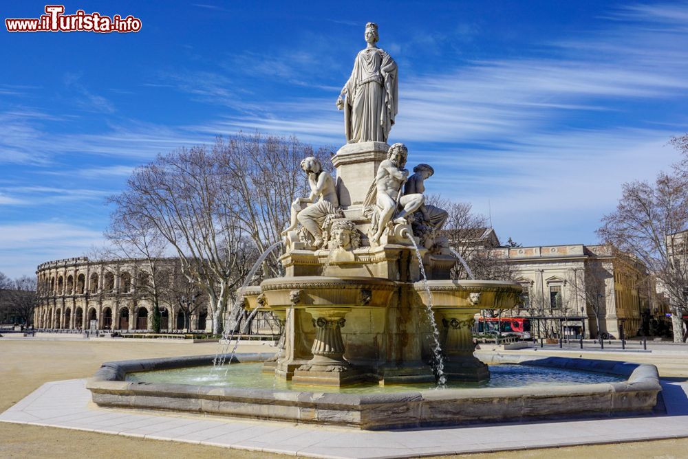 Immagine Nimes (Francia) in una giornata di sole con il cielo blu. Al centro dell'immagine, una antica fontana nella piazza antistante l'arena romana.