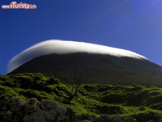 Immagine E' una di quelle nubi che si forma quando una massa d'aria calda incontra una catena montuosa e viene forzata a risalirla. La nube orografica, che deriva il suo nome dal prefisso di origine greca oros cioè monte, si forma tipicamente in alta montagna in seguito all'intenso riscaldamento del suolo roccioso nelle giornate serene, con alta pressione estiva. In questa immagine, una nuvola orografica lenticolare, che risulta immobile nel cielo fino alla sua dissipazione anche se in realtà è caratterizzata da un flusso che cambia continuamente, circonda con la sua forma bizzarra la cima della montagna Pico - © Ana Margarida / Shutterstock.com