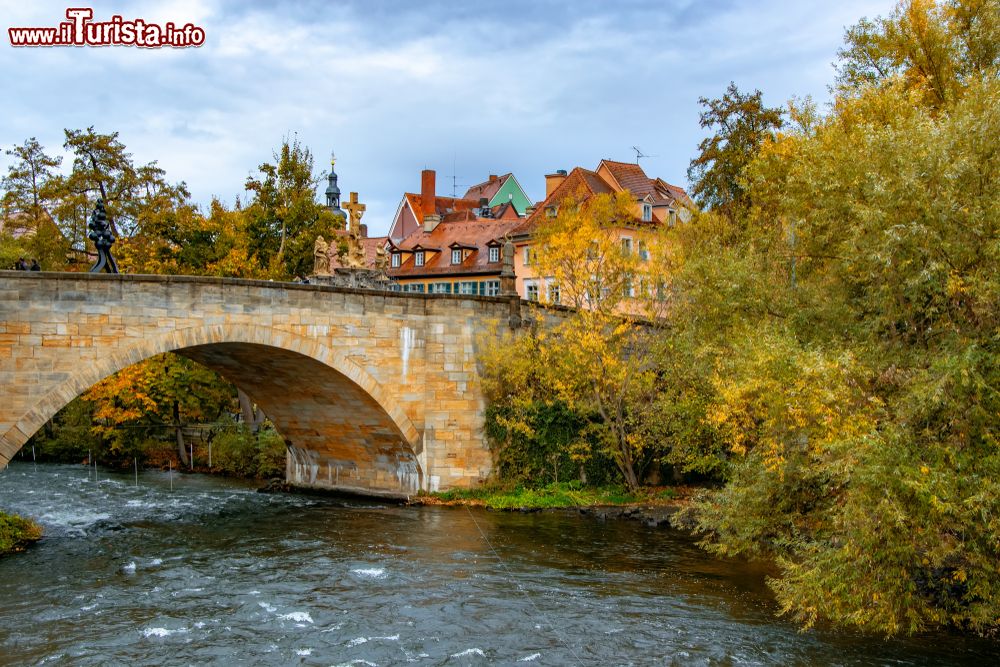 Immagine Paesaggio autunnale lungo il fiume Regnitz a Bamberga, Germania. Il ponte in pietra con il monumento alla crocifissione.