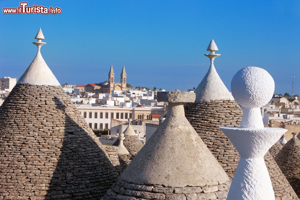 Immagine Panorama sui tetti dei trulli di Alberobello, Puglia, in una giornata di sole. Sullo sfondo, la skyline della cattedrale cittadina.