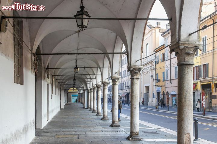 Immagine L'elegante portico di una via del centro di Parma - via della Repubblica, nel cuore del centro storico di Parma, presenta un'elegante fila di portici bianchi che conferiscono un maestoso contegno alla via e si pongono come baluardo di arte e storicità in contrasto ai negozi e al traffico tipici della città odierne. - © iryna1 / Shutterstock.com