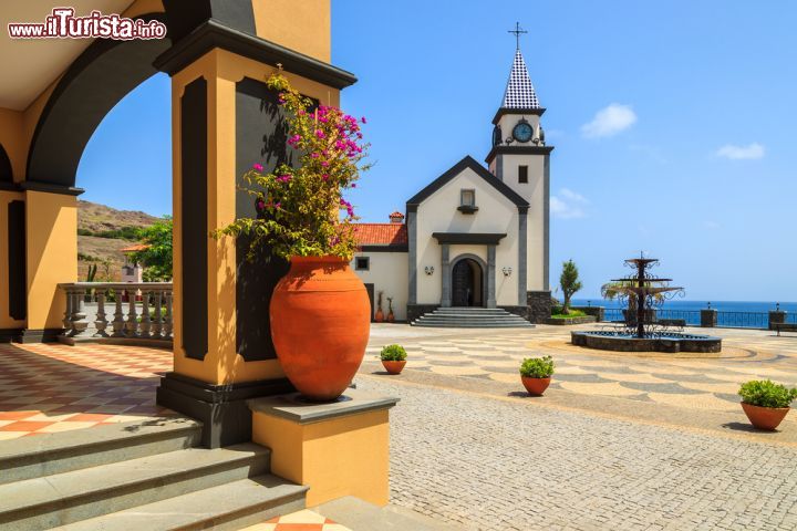 Immagine Piazza con Chiesetta dell'Isola di Madeira (Portogallo) - Essendo Madera conosciuta in tutto il mondo anche per il Flower Festival, le sue piazze riflettono tutto il buon gusto della primavera, anche in corrispondenza del piccolo edificio ecclesiastico del paese. La particolarità di questa piazza, infatti, è data dai vasi di ceramica dal color arancione alle cui estremità spuntano fiori meravigliosamente lilla, verdi o bianchi, che con il blu del cielo e l'azzurro dell'oceano di sfondo, regalano un vero e proprio tocco inebriante sia per la visione che per lo spirito - © Pawel Kazmierczak / Shutterstock.com