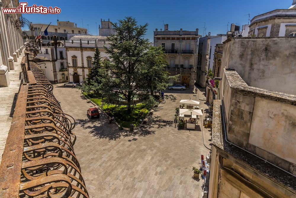 Immagine Piazza Roma a Martina Franca, Puglia, in estate. A quest'area urbana, con forma triangolare, si accede attraverso l'arco di Santo Stefano. Qui si affacciano importanti edifici storici oltre alla fontana dei Delfini situata al centro.