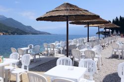 Caffè a Salò sul Lago di Garda, Lombardia. All'ombra degli ombrelloni di paglia, o sotto i raggi del sole, ci si può accomodare di fronte al lago di Garda per assaporare ...