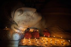 Giovani monaci buddhisti pregano in un tempio di Bagan, Myanmar. Con la luce delle candele tre giovani religiosi del sudest asiatico pregano in un luogo di culto della città di Bagan ...