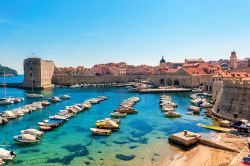 La baia di fronte alla città di Dubrovnik, Croazia, in una bella giornata di sole. A fare da cornice sono le mura fortificate e le barche ormeggiate al porto.

