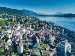 La città di Zugo fotografata dall'aereo, Svizzera. Si adagia sull'omonimo lago ed è sovrastata dall'imponente monte Zugerberg che s'innalza per 1039 metri.

