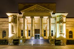 La facciata della biblioteca di Wuppertal, Germania, fotografata di notte. L'architettura è tipicamente in stile greco antico con quattro colonne che sorreggono il frontone decorato.
 ...