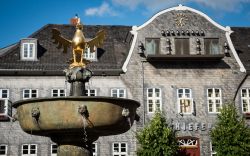 La fontana nella piazza centrale di Goslar (Germania) con l'aquila imperiale sulla cima. Sullo sfondo, un palazzo con campane e orologio - © pxl.store / Shutterstock.com