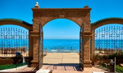 La spiaggia di Marina d'Or vista attraverso gli archi del cancello d'ingresso, Spagna. A lambire le coste di questo tratto litoraneo del sud spagnolo sono le acque trasparenti e azzurro ...