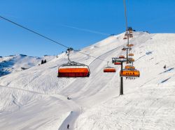 Skilift con seduta arancione sulle piste di Saalbach Hinterglemm, Alpi austriache (Tirolo). Saalbach è una rinomata stazione sciistica specializzata nello sci alpino.
