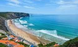 Spiaggia estiva di Arrifana nei pressi di Aljezur, Portogallo. Le rovine della fortezza, costruzione araba del XII° secolo, racchiudono una bella spiaggia frequentata dagli amanti del surf ...