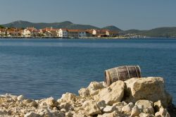 Un antico barile in legno fra le rocce del litorale nei pressi di Bibinje, Croazia. Sullo sfondo, il panorama della città.
