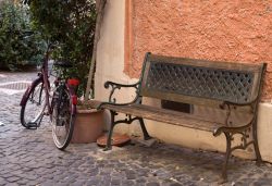 Un grazioso scorcio del borgo antico di Trevignano Romano, Lazio. Una panchina in legno con decorazioni intrecciate in ferro e una bicicletta. 
