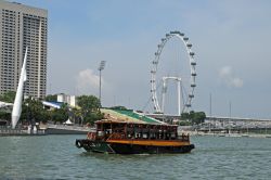 Una bumboat, tipica imbarcazione di legno a motore di Singapore, con la ruota panoramica sullo sfondo. Una volta arrivati a The Quays (i moli) ci si può imbarcare per una crociera di ...