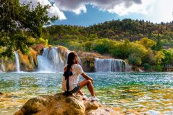Una giovane donna ammira il paesaggio nel Krka National Park di Skradin, Croazia, in estate. Sullo sfondo, le cascate che rendono celebre questo luogo.

