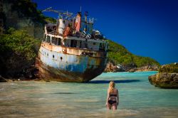 Una ragazza bionda in bikini nelle acque del mare Caraibico a Anguilla. Sullo sfondo ciò che resta di una nave naufragata vicino alla spiaggia.

