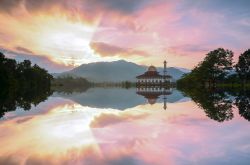 Veduta della moschea di Darul Quran al tramonto, Selangor, con i riflessi sull'acqua del lago.



