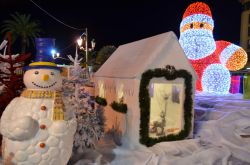 Pupazzo, capanna e statua di Babbo Natale illuminato, in una foto notturna al villaggio natalizio di Place de Gaulle, Ajaccio
