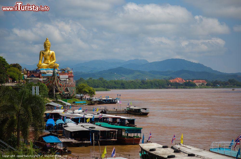 Immagine Statua dorata di Buddha a Chiang Saen, Thailandia. In primo piano, barche ormeggiate sull'acqua fangosa  - © opportunity_2015 / Shutterstock.com