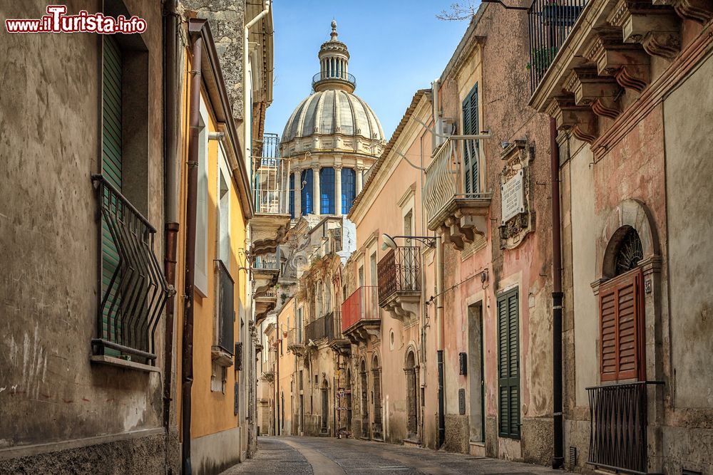 Immagine Stretta via di Ragusa, Sicilia, Italia. Un suggestivo scorcio fotografico della città con le vecchie case che si affacciano sulla strada e il duomo della chiesa visibile sullo sfondo.